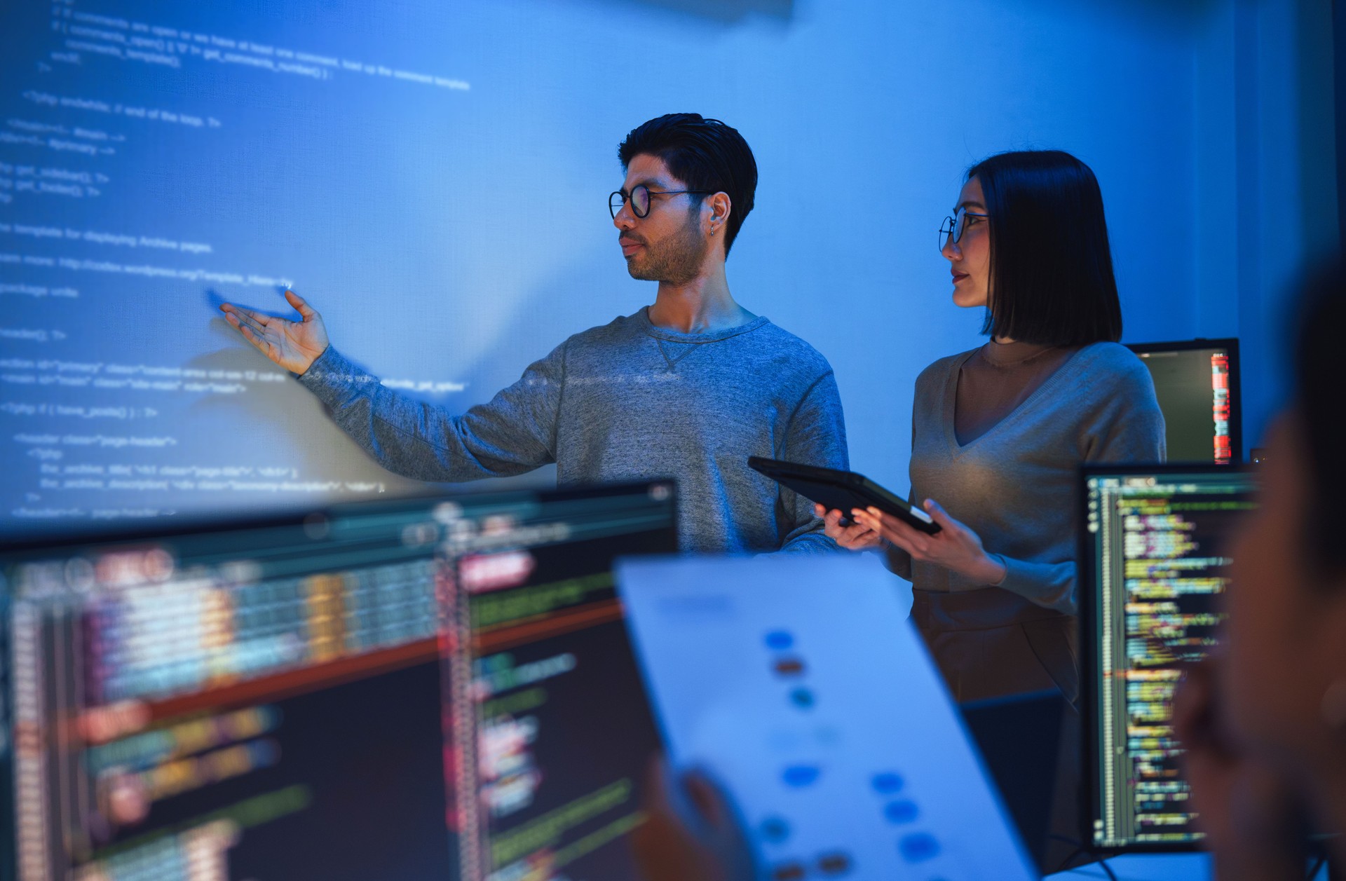 asian developer leads present code review session, pointing at code projected on the wall with colleagues  teamwork and knowledge sharing in software development.